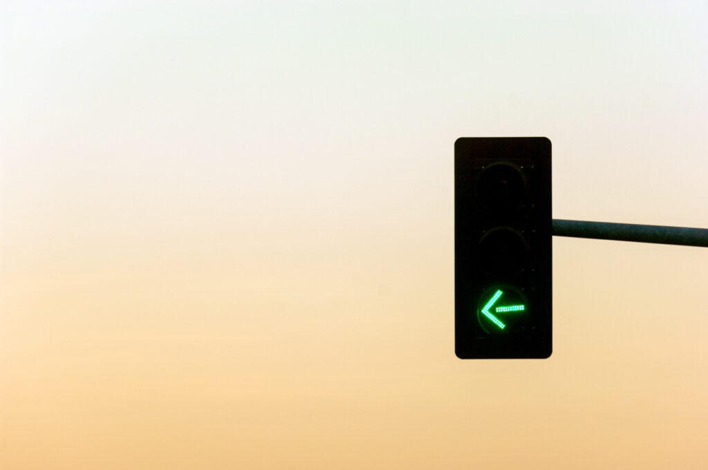 Traffic light on crossroads with green light arrow and sunset on the background
