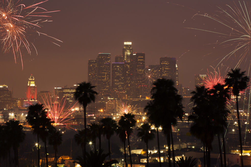 Fireworks exploding over the Downtown Skyline, framed by palm trees.