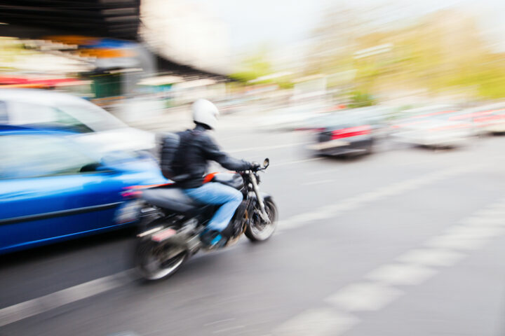 driving motorbike and cars on a city street. The photo was taken by panning the camera, so the vehicles are pictured in motion blur