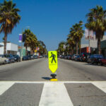 Perspective view down a street with stores, cars and palm trees from a pedestrian crosswalk in Venice Beach, near Los Angeles, California.